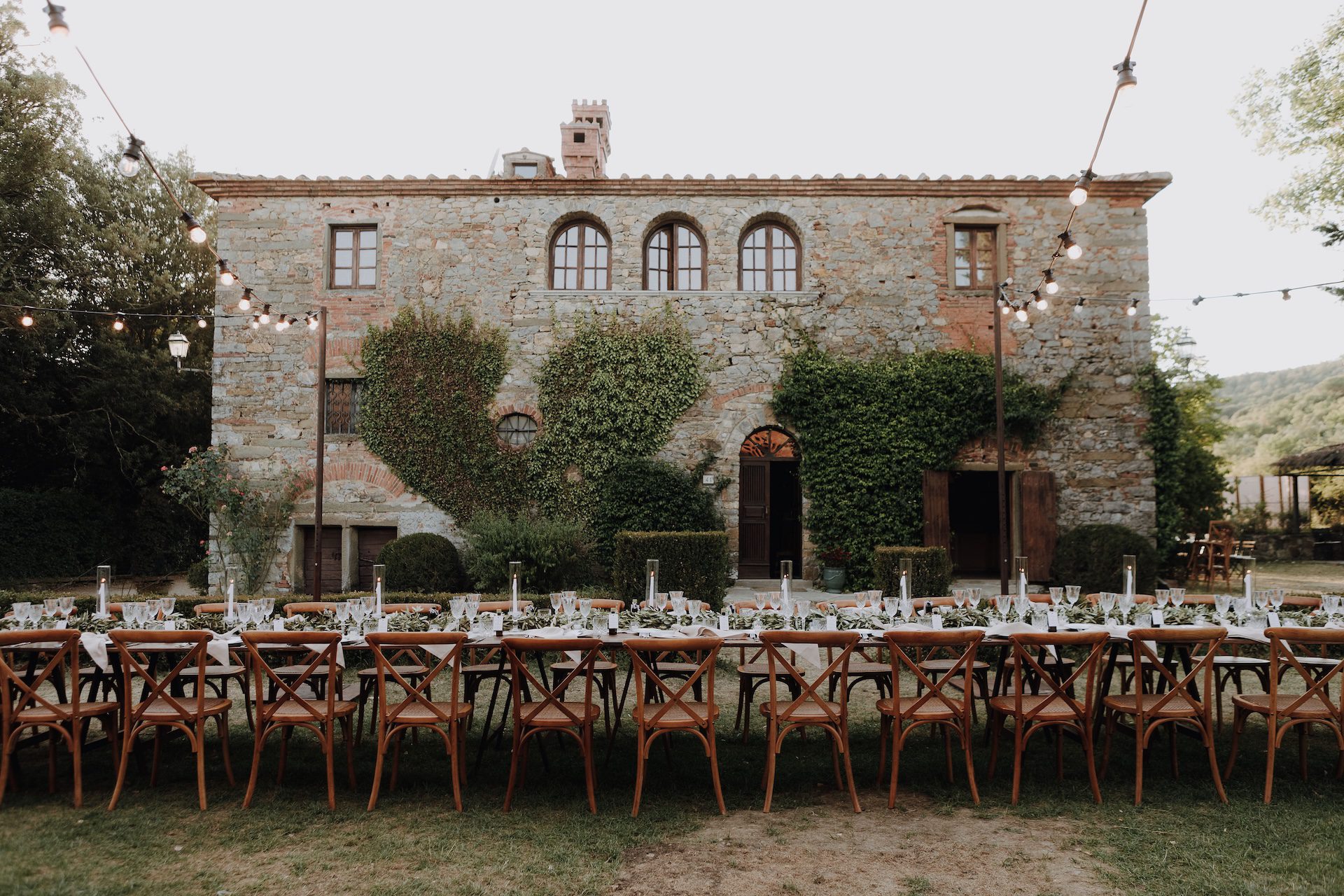 Tavola imperiale apparecchiata con mise en place in stile rustico e immersa nella campagna toscana